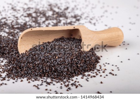 Poppy seed on the kitchen table. Spilled poppy seed and wooden spoon. White background.