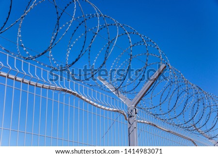 barbed wire on a metal fence against a blue sky
