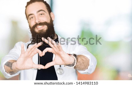 Doctor with long hair wearing medical coat and stethoscope smiling in love showing heart symbol and shape with hands. Romantic concept.