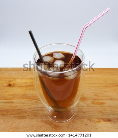 Iced tea with red and blue straw on wooden table, white background