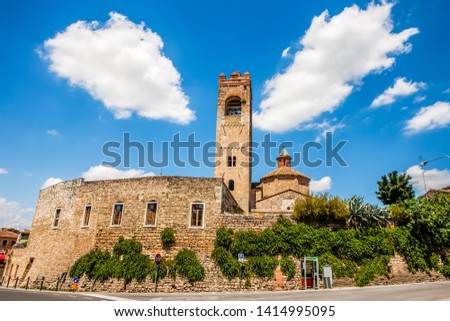 Stone walls of the Sant Agata colleggiate Church and his bell tower as it seen from the road with particular clouds in the blue sky. Asciano,Tuscany