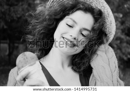A black and white portrait of a lovely, curly-haired, smiling with the teeth girl in straw hat with the ice cream cone in her hand  Royalty-Free Stock Photo #1414995731