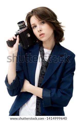 Beautiful brunette girl in a jacket and jeans posing on a white background with an old vintage movie camera, in isolation
