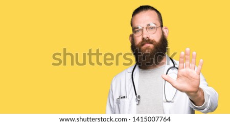 Young blond doctor man with beard wearing medical coat doing stop sing with palm of the hand. Warning expression with negative and serious gesture on the face.
