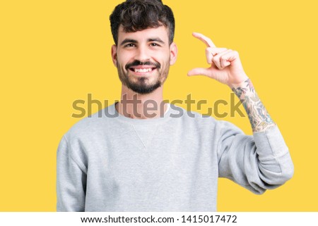 Young handsome man wearing sweatshirt over isolated background smiling and confident gesturing with hand doing size sign with fingers while looking and the camera. Measure concept.