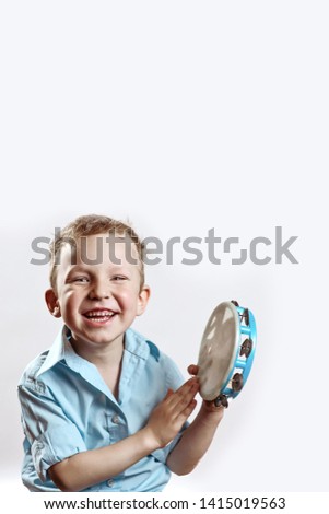 cheerful boy in a blue shirt holding a tambourine and smiling on a light background