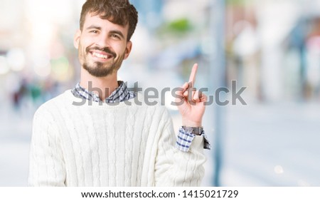 Young handsome man wearing winter sweater over isolated background with a big smile on face, pointing with hand and finger to the side looking at the camera.