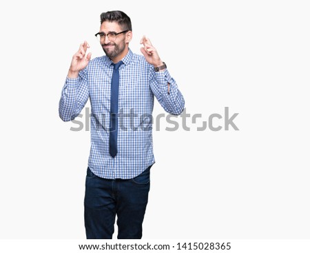 Young business man wearing glasses over isolated background smiling crossing fingers with hope and eyes closed. Luck and superstitious concept.