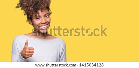 Beautiful young african american woman over isolated background doing happy thumbs up gesture with hand. Approving expression looking at the camera showing success.