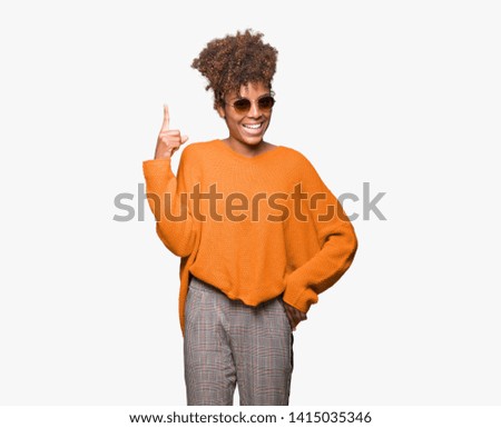 Beautiful young african american woman wearing sunglasses over isolated background pointing finger up with successful idea. Exited and happy. Number one.