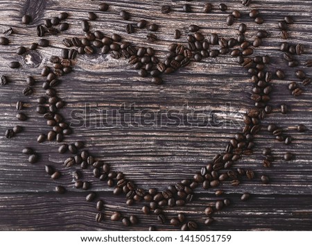 Heart shaped frame made of spilled coffee beans on a wooden table. Rustic stile. Top view.