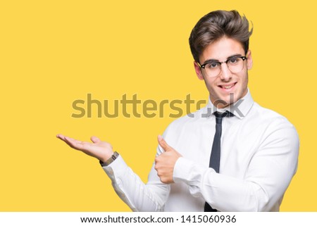 Young business man wearing glasses over isolated background Showing palm hand and doing ok gesture with thumbs up, smiling happy and cheerful