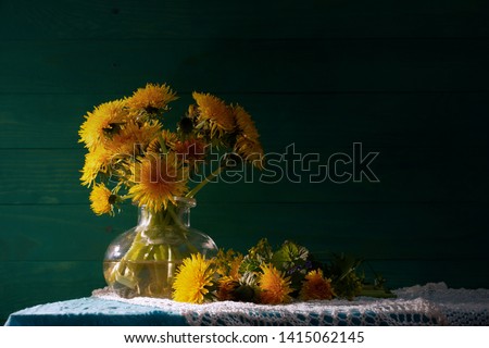 Dandelions in a glass vase. Bouquet of wilting dandelions. Green wooden background. Rustic still life