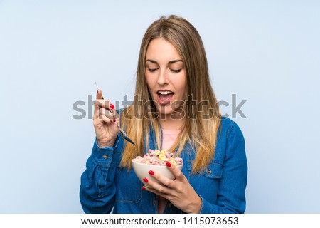 Young woman with bowl of cereals over isolated blue wall
