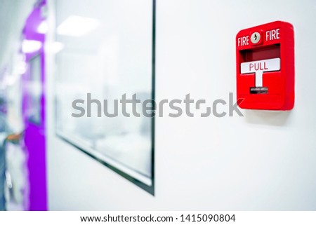 Fire alarm switch on the factory wall.Blurred background is the corridor, the office, the purple door.soft focus.