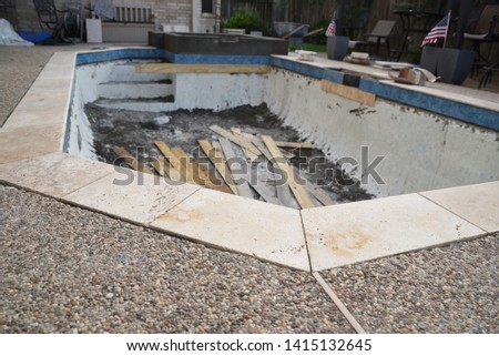 Swimming Pool remodel with construction material and trash lined with new blue tile and travertine coping