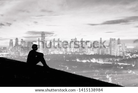 Thoughtful young man sitting on a hill looking at city view.