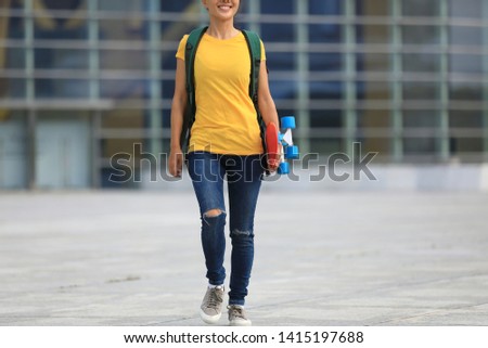 Woman skateboarder walking with skateboard in hand at city
