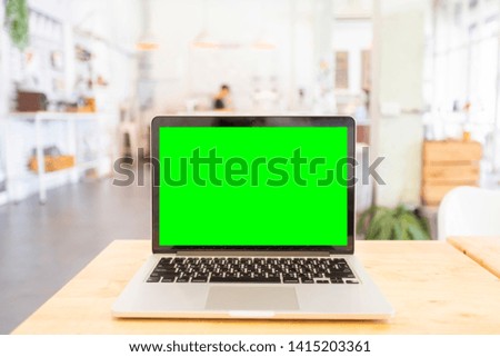 Mockup image of laptop with blank Green screen on wooden table of In the coffee shop.