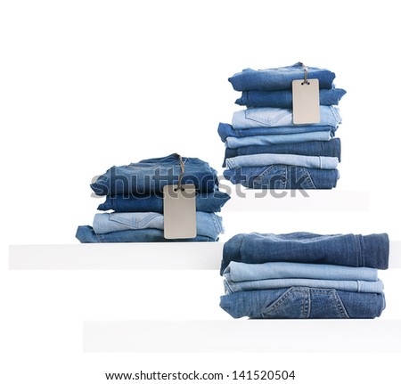 Pile of blue jeans with tag label on white shelf in shop.