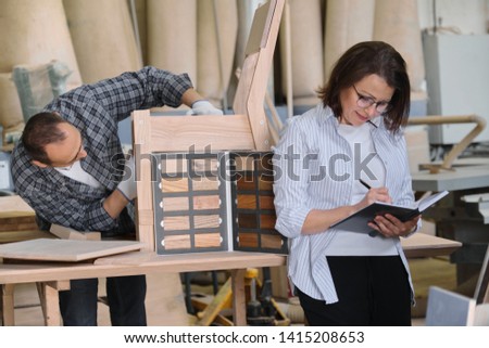 Furniture joinery production, working male joiner and female designer with wood samples choosing finishing, writing in business notebook.