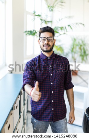 Handsome hispanic man working using computer and writing on a paper happy with big smile doing ok sign, thumb up with fingers, excellent sign