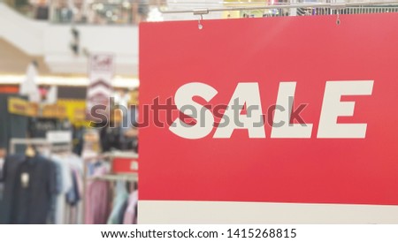 Sale label (tag), symbol of special promotion hanging in shopping mall as concept of offering product at reduced price. Blurred clothing department store background.