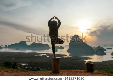 Happy man in black clothes doing yoga pose standing on the tree. Incredible sunset background with mountains and lakes. The concept of balance and harmony in life. Photo with noise. Selective focus