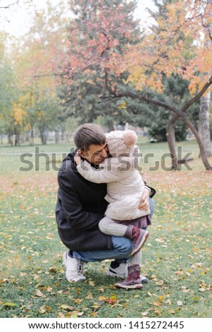 Child hugging and kissing their dad. Father smiles when his daughter ran up to him on the background of autumn park.