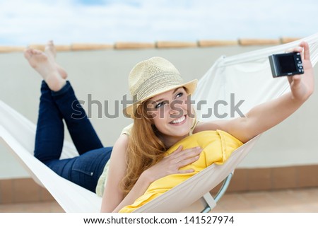 Happy and relaxed young woman photographing herself with digital camera in hammock