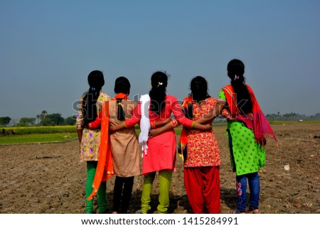 Close up back shot of five young girls, teenagers wearing colorful salwar kameez dress, looking up to the blue sky in a harvested field with the hands interlocking their waist in unity, conceptual pic
