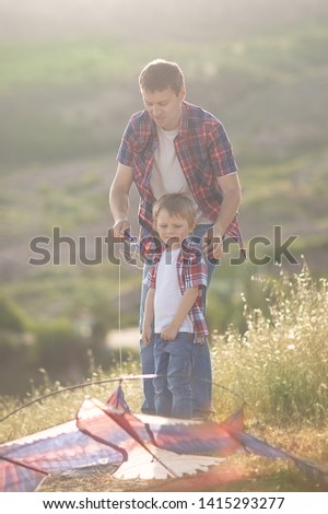 A little boy with his father in the beautiful hills flying a kite.