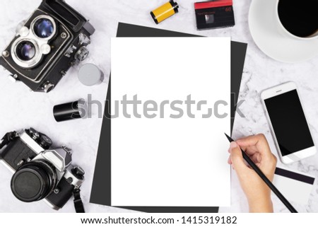 flat lay hand writing in a blank white page notebook decorated with vintage camera and photography tool on white marble background