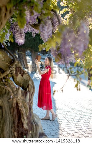 Girl in red dress smiling taking selfie picture in wisteria garden.
