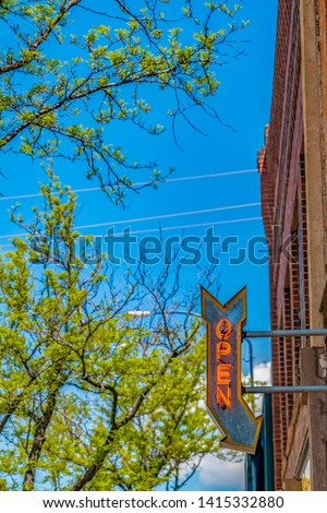 Open arrow sign on a building with vibrant trees and blue sky in the background