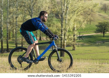 Cyclist in shorts and jersey on a modern carbon hardtail bike with an air suspension fork standing on a cliff against the background of fresh green summer forest