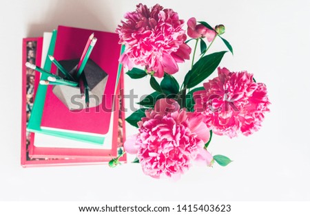 bouquet of pink peonies, a stack of books, pencils and a notebook on a white table, top view