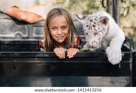 Portrait of a domesticated white tiger playing with a blonde child
