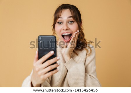Beautiful excited young woman wearing sweater standing isolated over beige background, having a video call