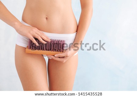 Beautiful young woman with cleaning brush on light background. Depilation concept