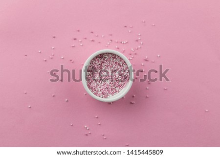 Sprinkles isolated on pink background - little white bowl with pearly pink cake topping sprinkles and some scattered on pink - top view