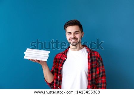 Handsome young man with books on color background
