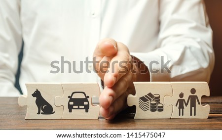 A man shares wooden puzzles with images of property, children and pets. The concept of divorce. The process of sharing property. Child custody and parental responsibility. Marriage contract Royalty-Free Stock Photo #1415475047