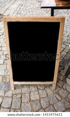 Empty eating menu advertising board. Blank blackboard outdoor advertising stand mock up template. Clear street signage / black chalkboard for slogan placed in outdoor dining area of restaurant / cafe.