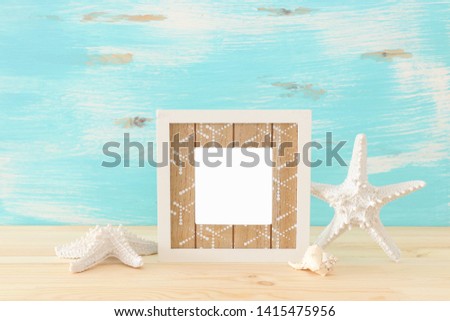 Nautical concept with empty photo frame and starfish over wooden table. For photography montage