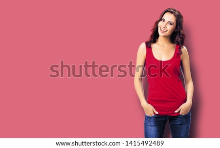 Portrait photo - young smiling woman in casual clothing, blue jeans. Red color background with copy space for some slogan or sign text. Happy beautiful brunette girl at studio.