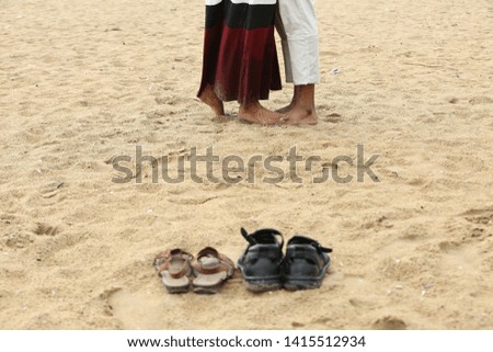 a young married couple standing on each other in beach sand with their slippers taken off 