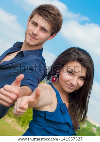 Happy teenage couple boy and girl showing thumbs up over blue sky background