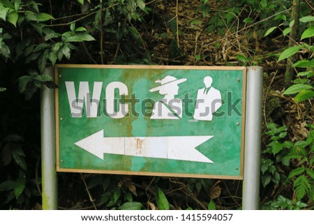 Rusted signboard "WC" in metal on green background with silhouettes of man and woman.