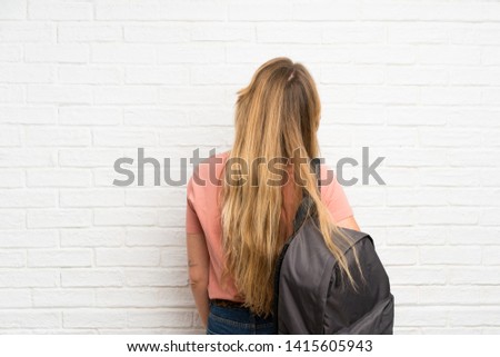 Young blonde woman over white brick wall with backpack